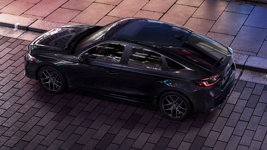 Overhead side view of black Honda Civic Hatchback parked at a curb on a brick road.