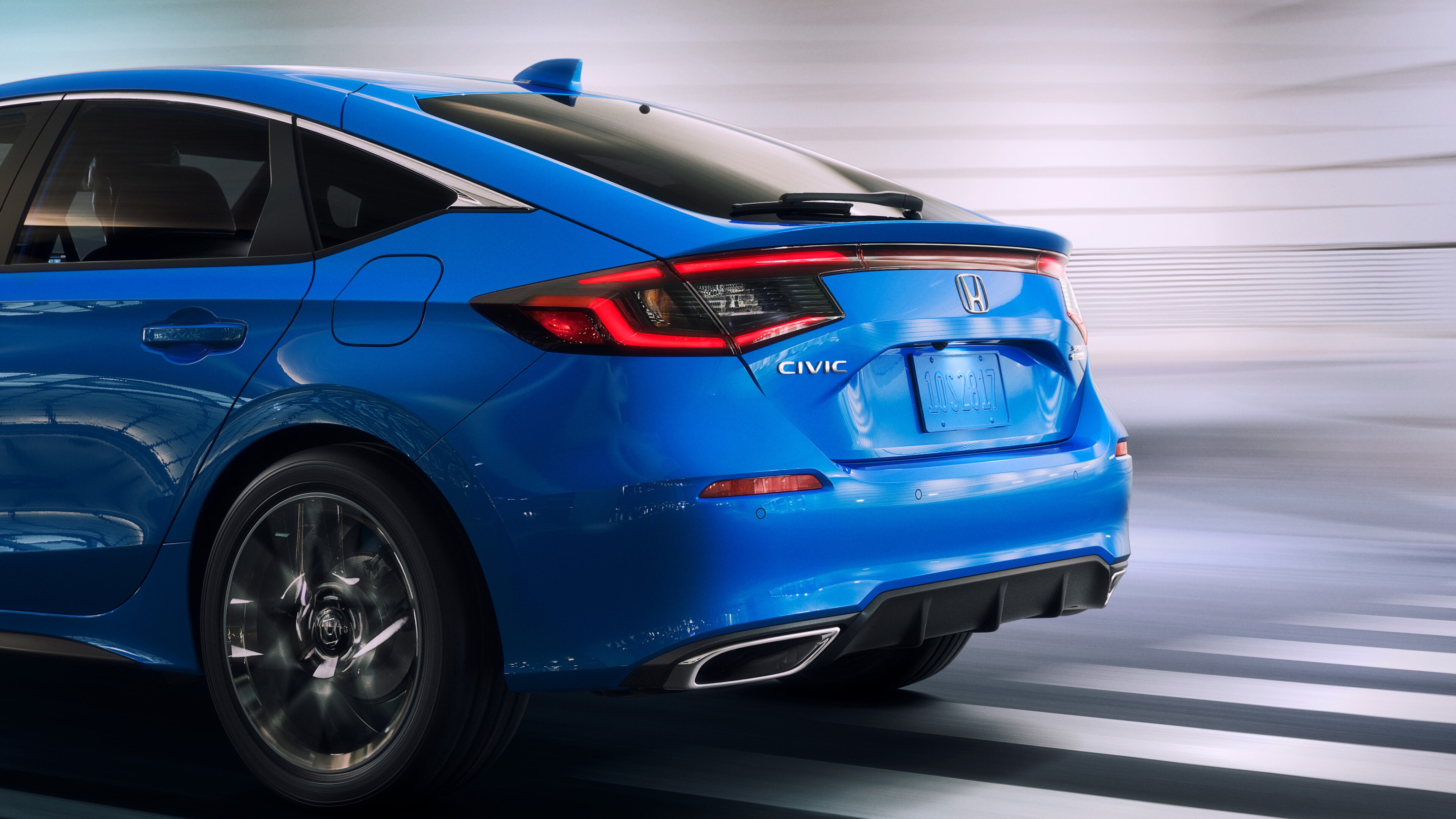 Side rear view of blue Honda Civic Hatchback driving over a white-striped road with blurred background