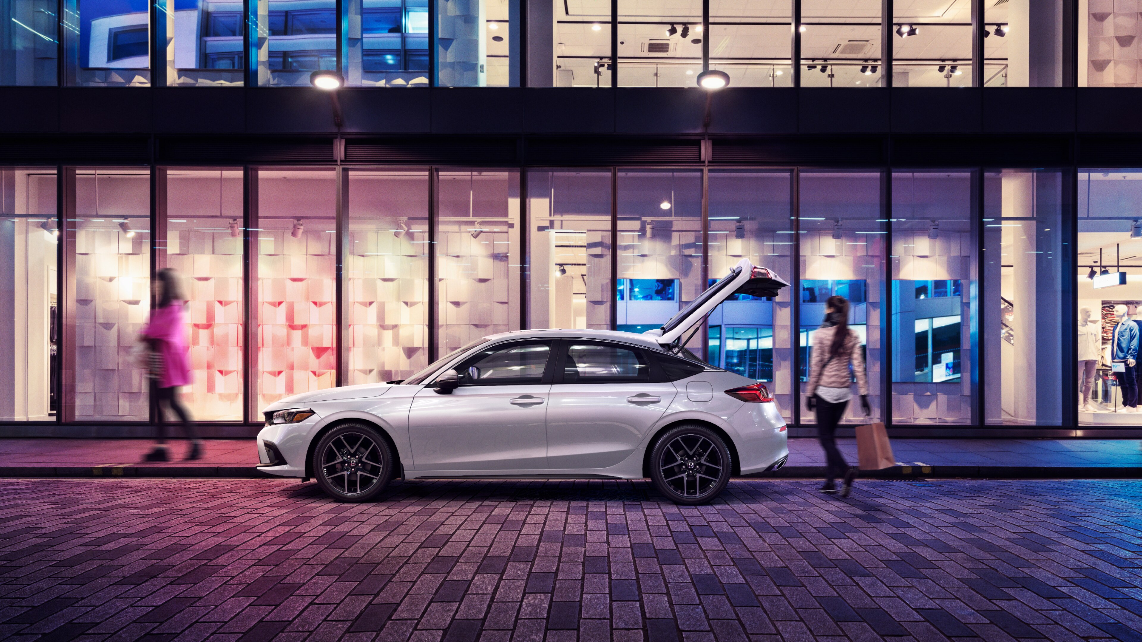 Side view of white Honda Civic Hatchback parked at a curb at night with rear door open