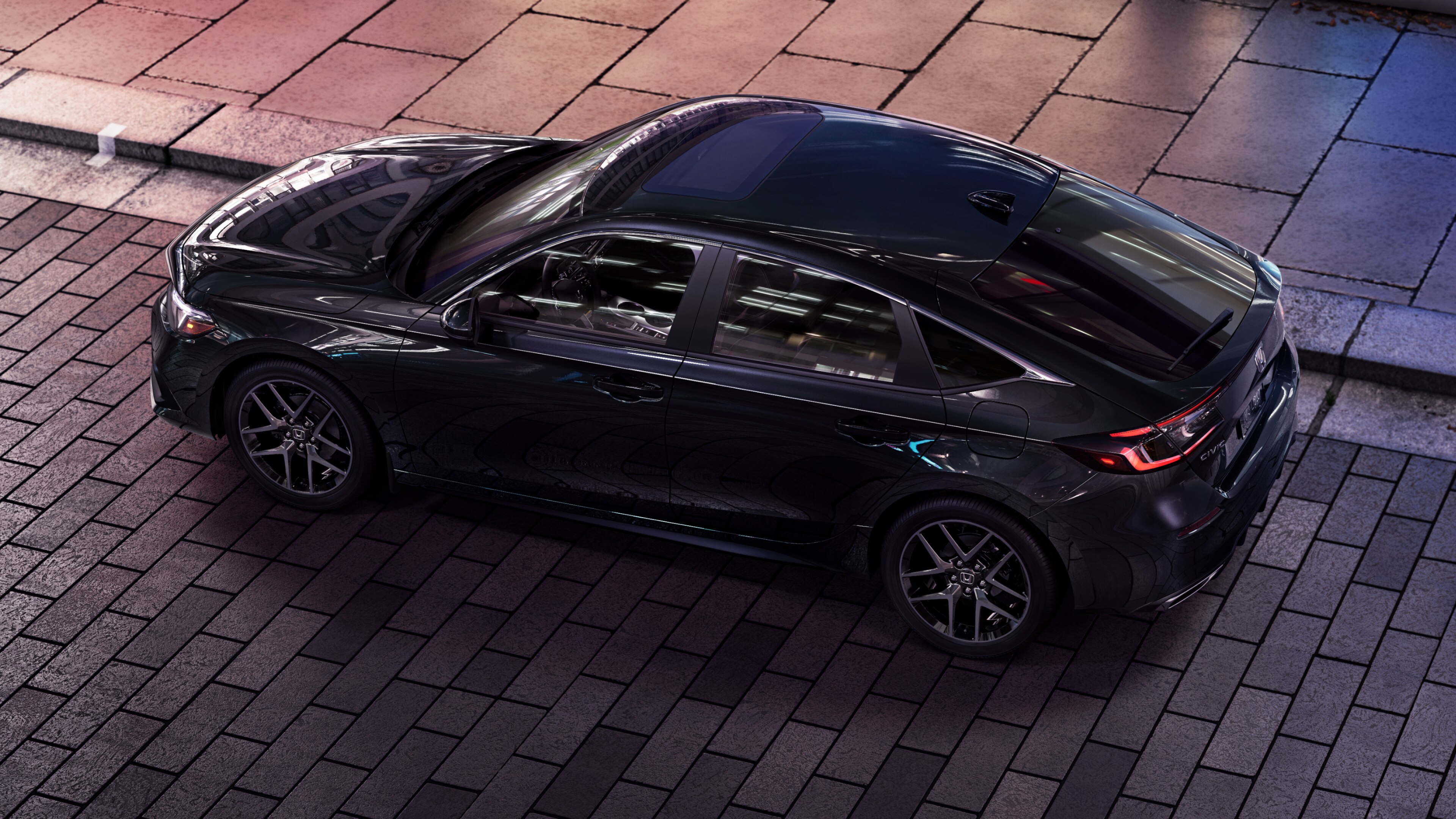 Overhead side view of black Honda Civic Hatchback parked at a curb on a brick road.