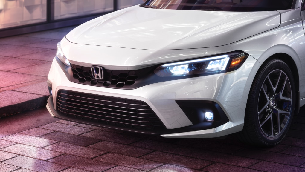 Side-angled close-up of white Honda Civic Hatchback with headlights shining on a brick road